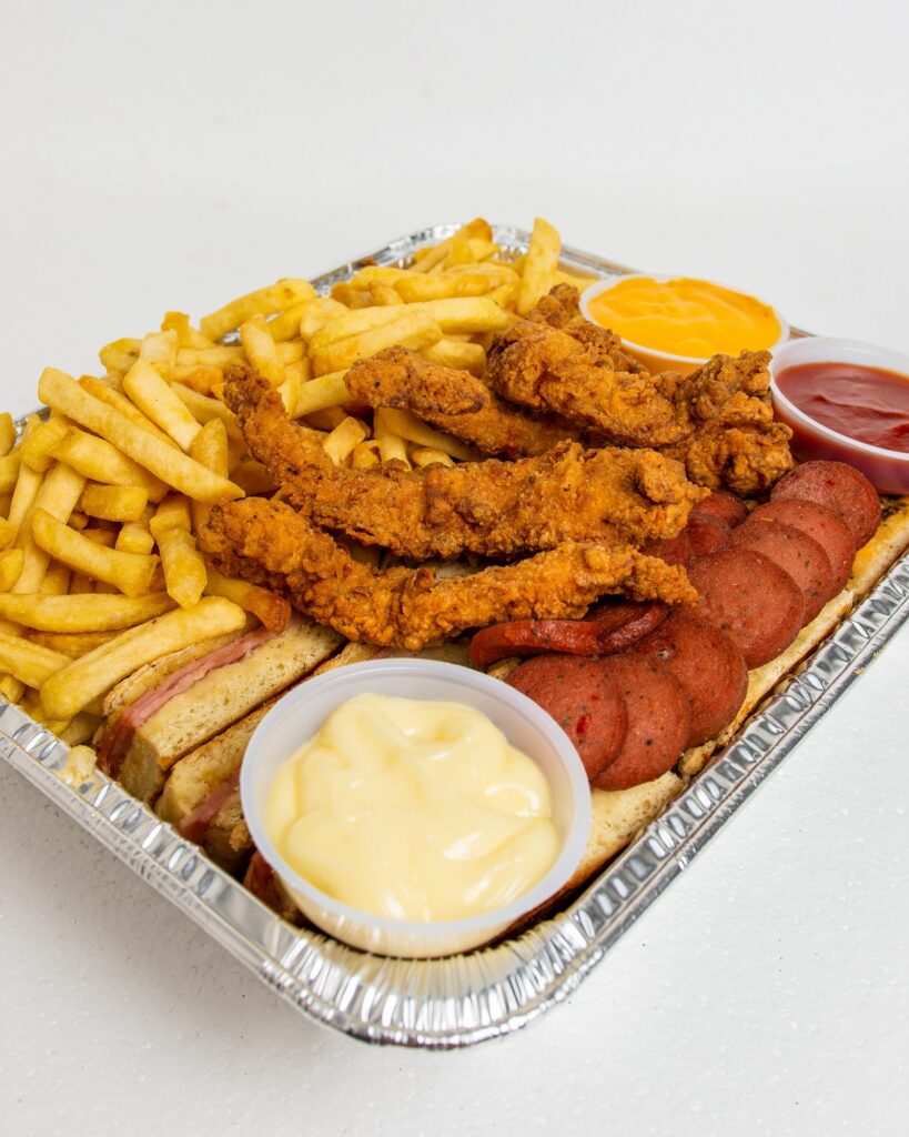 Bandeja RiQUi's para compartir: papas fritas, dedos de pollo apanados y salchicha sobre pan, con salsas de queso, tomate y mayonesa