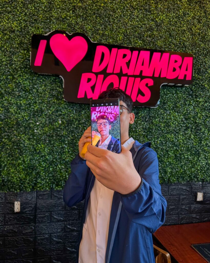 Un cliente se toma una foto con su batido frente al rótulo I love Diriamba RiQUi's